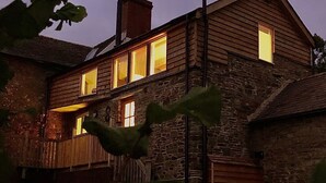A stone building with wooden siding and multiple lit windows, suggesting a cozy interior.