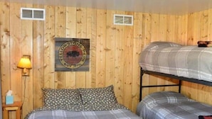 Ein Zimmer mit Holzwänden, einem Bett mit karierter Decke, einem Stockbett, einer Wandlampe und einem Schild mit einem Büffel.