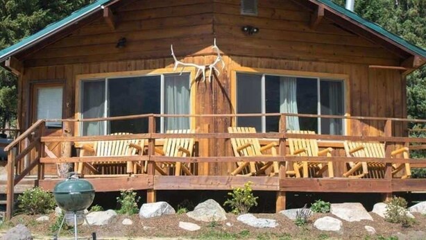 Eine Holzhütte mit Veranda, großen Fenstern und einem Grill.