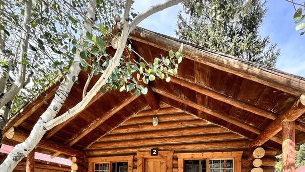 A rustic log cabin with a porch, wooden benches, and a number '2' sign. - Comfy cabin is situated on the Silver Gate property which overlooks 10,000ft tall mountain peaks surrounding the town. (Silver Gate)