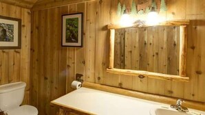 A wooden cabin bathroom with a white sink, a mirror, and framed pictures on the wall. - Comfy cabin is situated on the Silver Gate property which overlooks 10,000ft tall mountain peaks surrounding the town. (Silver Gate)