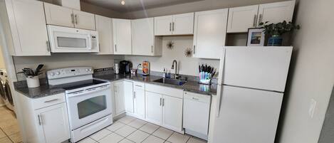 A kitchen with white cabinets, a microwave, stove, dishwasher, and a refrigerator.