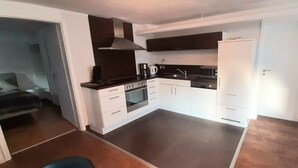 Una cucina compatta con mobili bianchi, forno a incasso, fornello e macchina per il caffè.