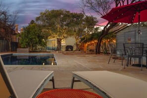 Un patio trasero con piscina, sillas de descanso y una sombrilla roja.