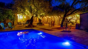 A swimming pool with lights, outdoor seating, and trees.