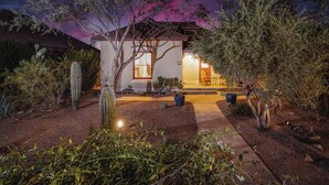 A house with a well-lit front porch, surrounded by various cacti and shrubs.