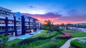 Un hôtel moderne à plusieurs étages, doté d’un jardin aménagé et offrant une vue sur le coucher de soleil.