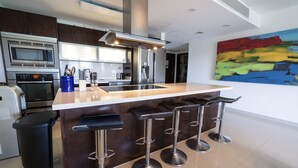Une cuisine moderne dotée d’un îlot central, d’appareils électroménagers en acier inoxydable et d’un tableau abstrait aux couleurs vives accroché au mur.