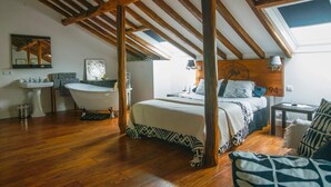 Ein Schlafzimmer mit Holzboden, einem Bett, einem Nachttisch, einer Lampe und Blick auf den Himmel durch ein Dachfenster.