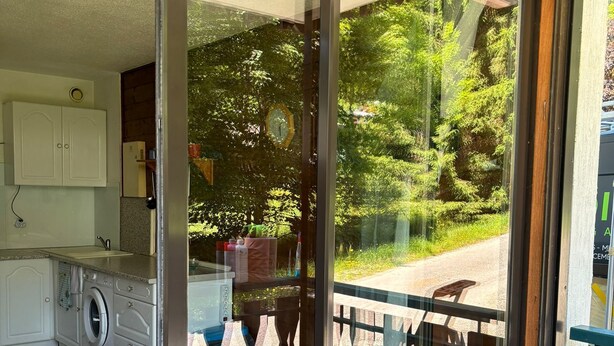 Une cuisine moderne équipée d’un lave-linge, un coin repas avec une table et des chaises, et un balcon offrant une vue sur la verdure.