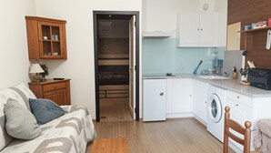 Un espace de vie compact comprenant un canapé, une table en bois, un lave-linge et un coin cuisine.