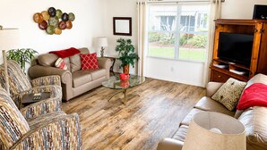 A living room with a sofa, armchairs, a coffee table, a TV stand, a ceiling fan, and a window with blinds. - CLEAN, CLEAN, CLEAN; Walk to pools; Golf Cart Included; NO Xtra guest fees !!! (The Villages)