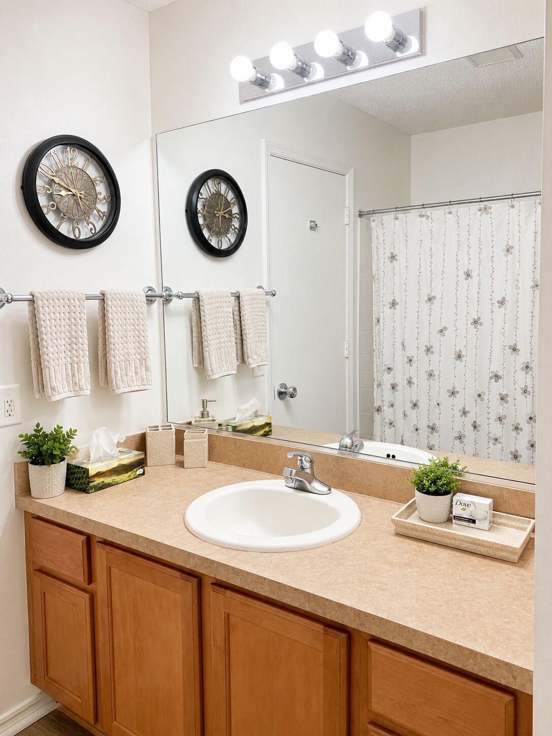 A bathroom with a sink, mirror, two wall clocks, and a shower curtain.