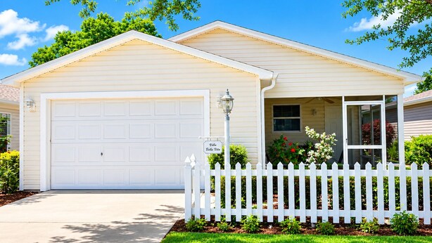 A single-story house with a white garage, a small porch with a white picket fence, and a clear blue sky. - CLEAN, CLEAN, CLEAN; Walk to pools; Golf Cart Included; NO Xtra guest fees !!! (The Villages)