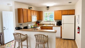 A compact kitchen with wooden cabinets, a white refrigerator, a microwave, a gas stove, and a sink. There are two wicker chairs at the counter. - CLEAN, CLEAN, CLEAN; Walk to pools; Golf Cart Included; NO Xtra guest fees !!! (The Villages)