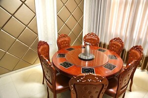 Una mesa de comedor redonda de madera con seis sillas tapizadas, un adorno central y un papel tapiz estampado en el fondo.
