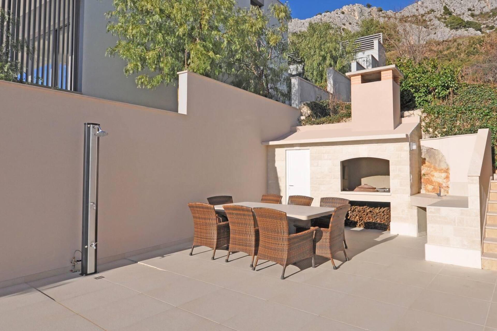 Une terrasse extérieure avec une table et des chaises, un barbecue intégré et une douche.