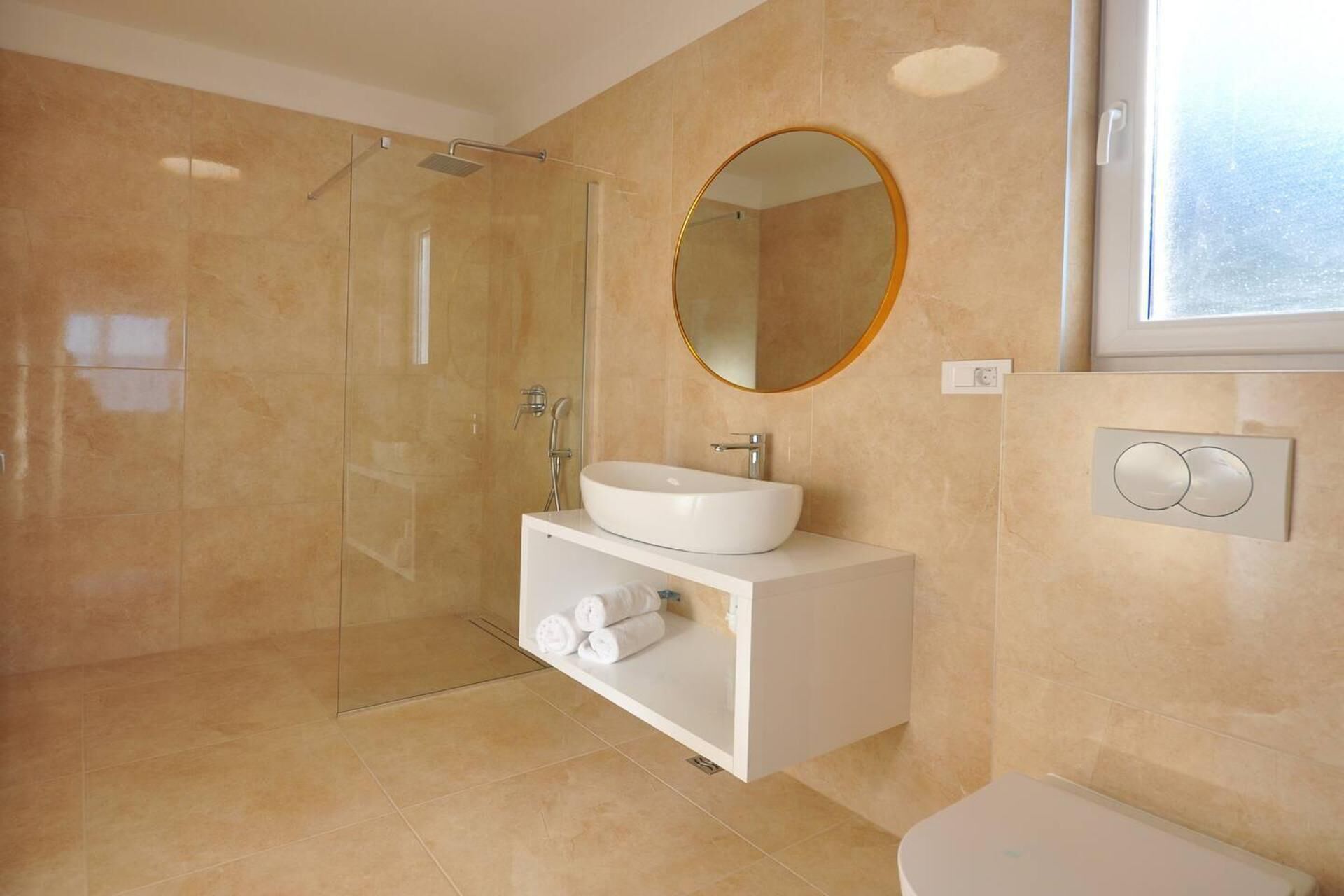A modern bathroom with a glass-enclosed shower, a white sink, and a round mirror.