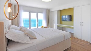 A modern bedroom with a large bed, a TV mounted on a yellow wall, and a view of the sea through large windows. - Villa Iva With sea View and Pool (Omis)