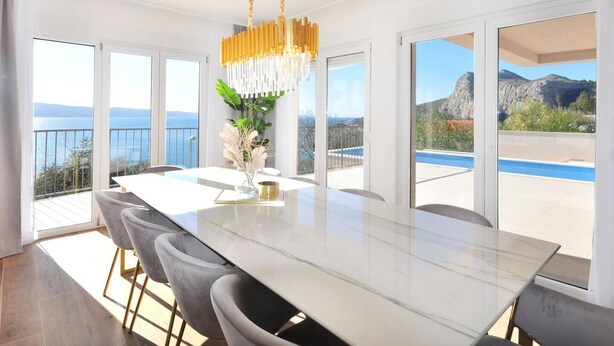 A modern dining area with a large table, comfortable chairs, and a decorative chandelier. - Villa Iva With sea View and Pool (Omis)