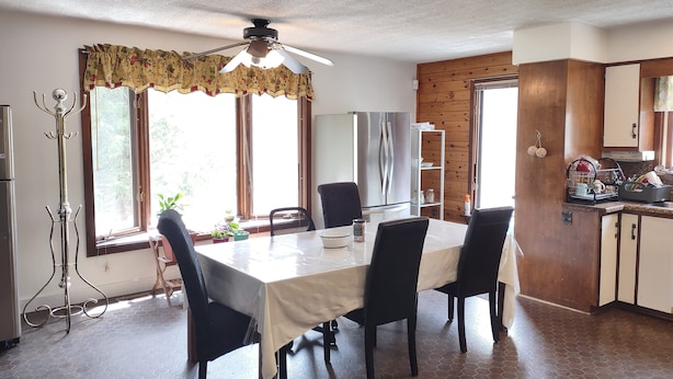 A dining area with a table set for four, a ceiling fan, a refrigerator, and a wooden wall.