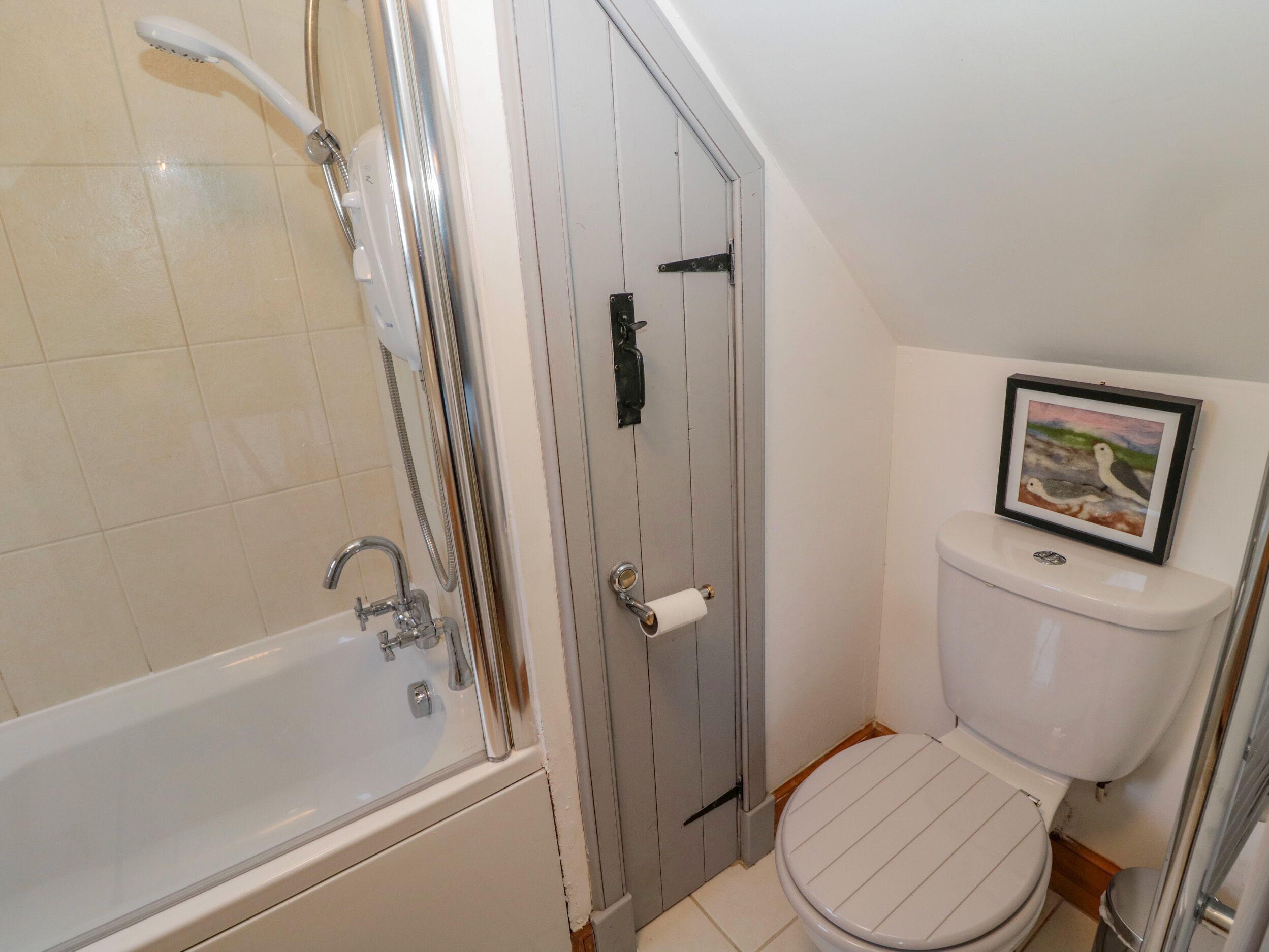 A bathroom with a bathtub, toilet, and a framed picture on the wall.