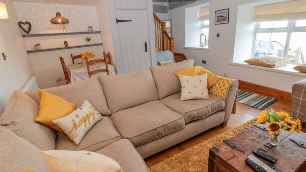 A cozy living room with a beige sofa, yellow cushions, a wooden coffee table with remote controls, and a staircase leading to another room. - Twincote (Wooler)