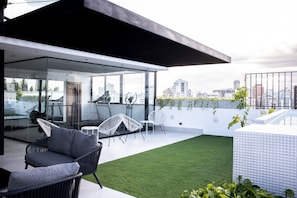 Eine moderne Dachterrasse mit Glaswänden, Sitzgelegenheiten im Freien und Blick auf die Stadtlandschaft.