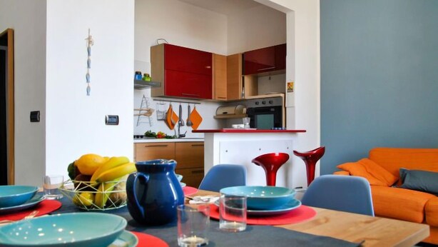 A modern living room with a dining area, featuring a kitchen in the background with red cabinets and a white countertop. - Sotto Il Segno Dei Pesci by Interhome (Formia)