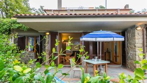 Un patio con mesa y sillas, una sombrilla azul y un muro de piedra.