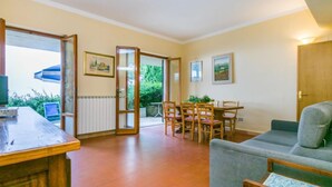 Una sala de estar con sofá, una mesa de comedor con sillas, televisión y vistas al exterior.