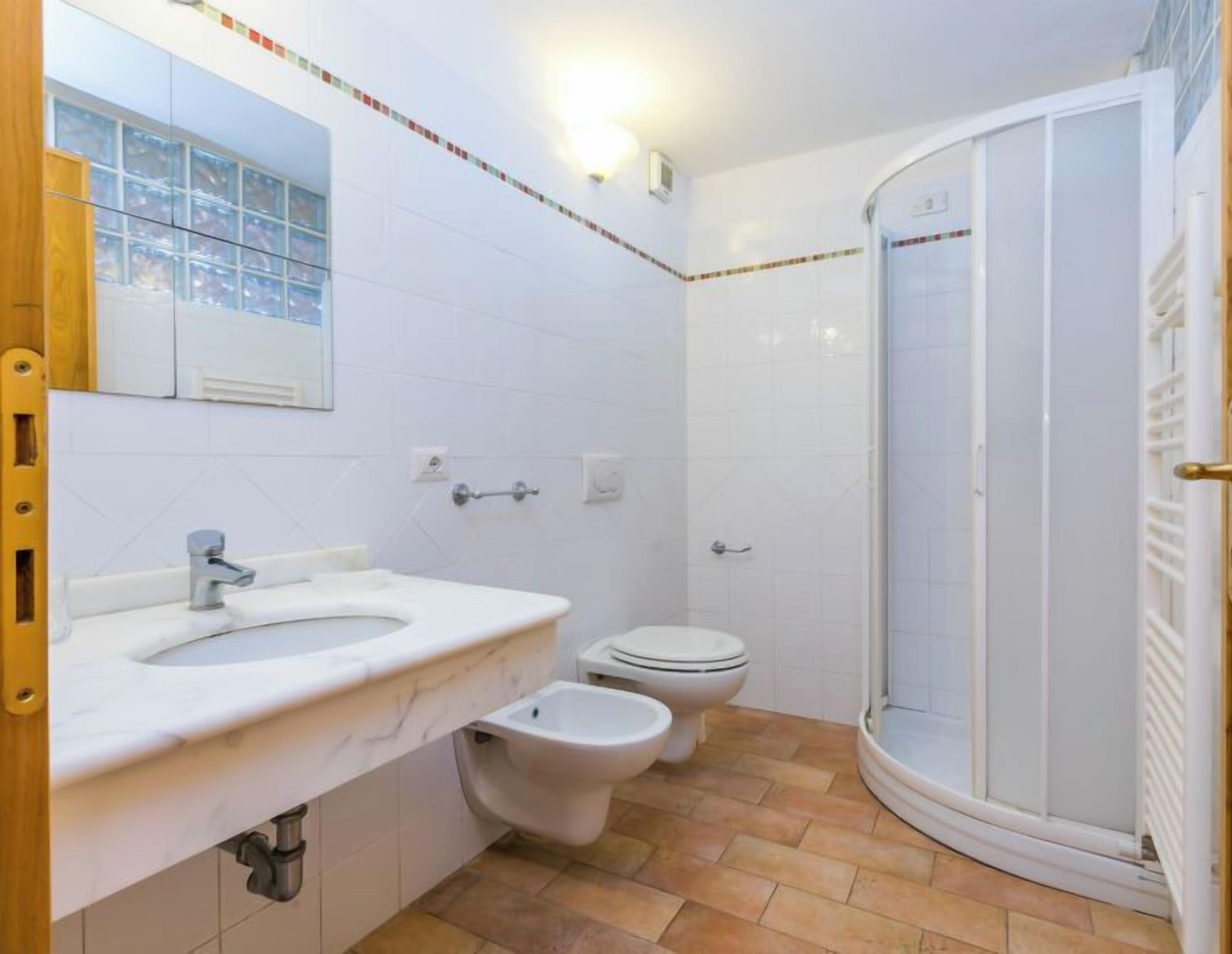 A bathroom with a white sink, two toilets, a shower, and a tiled floor.