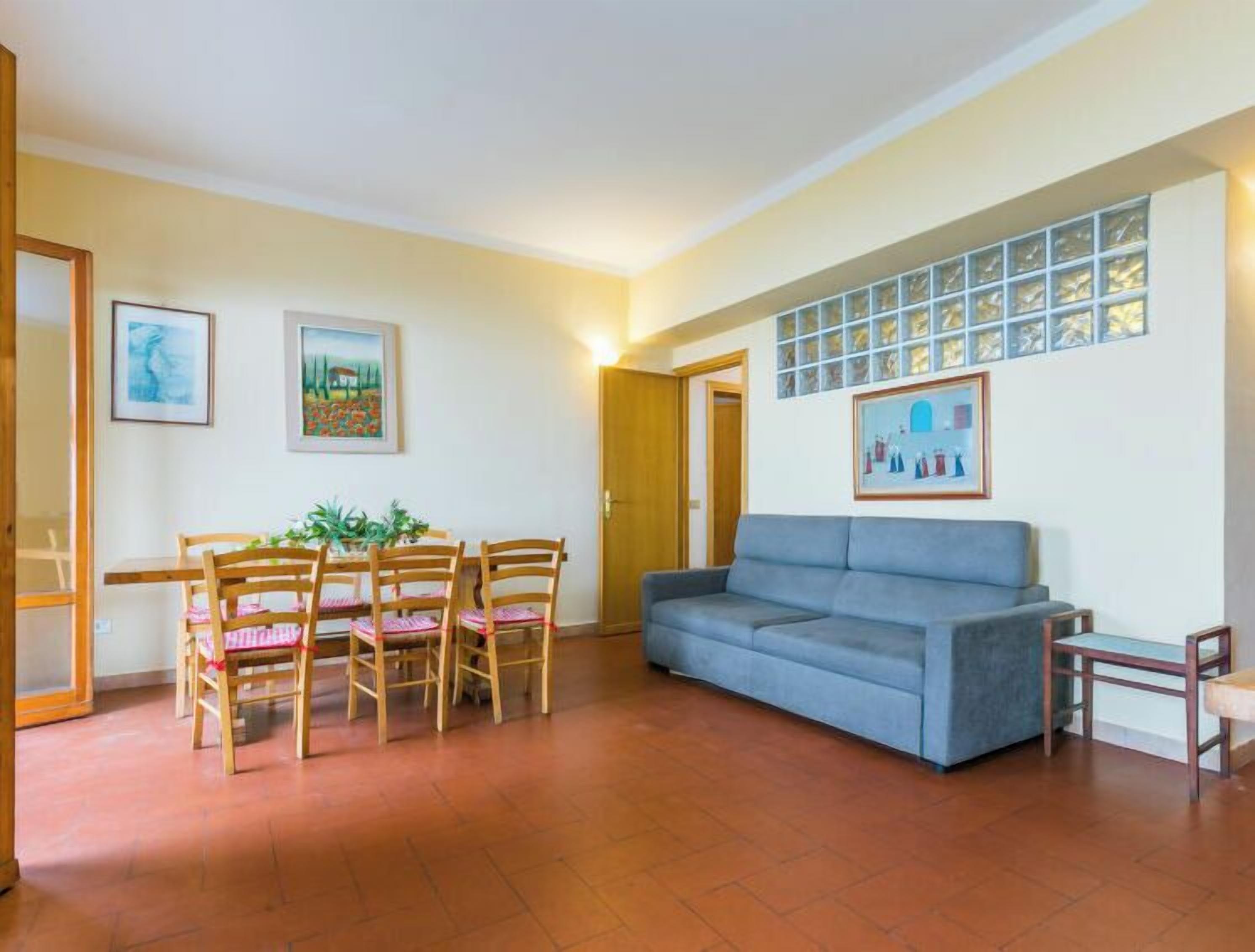 A living room with a blue sofa, wooden dining table with chairs, and two framed pictures on the wall.