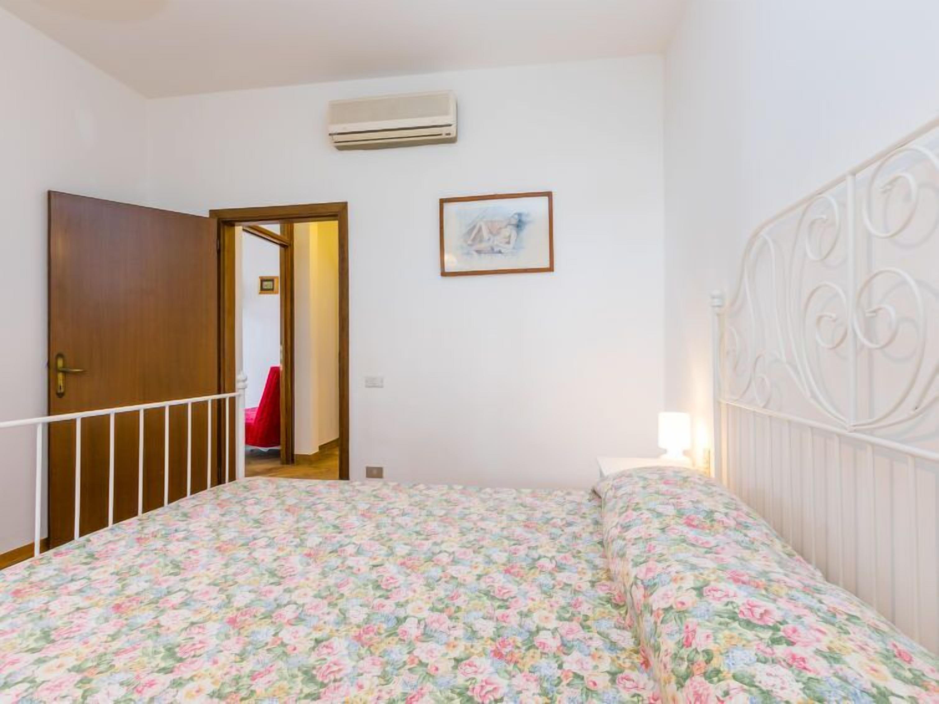 A bedroom with a floral bedspread, a white metal headboard, a door, and a framed picture on the wall.