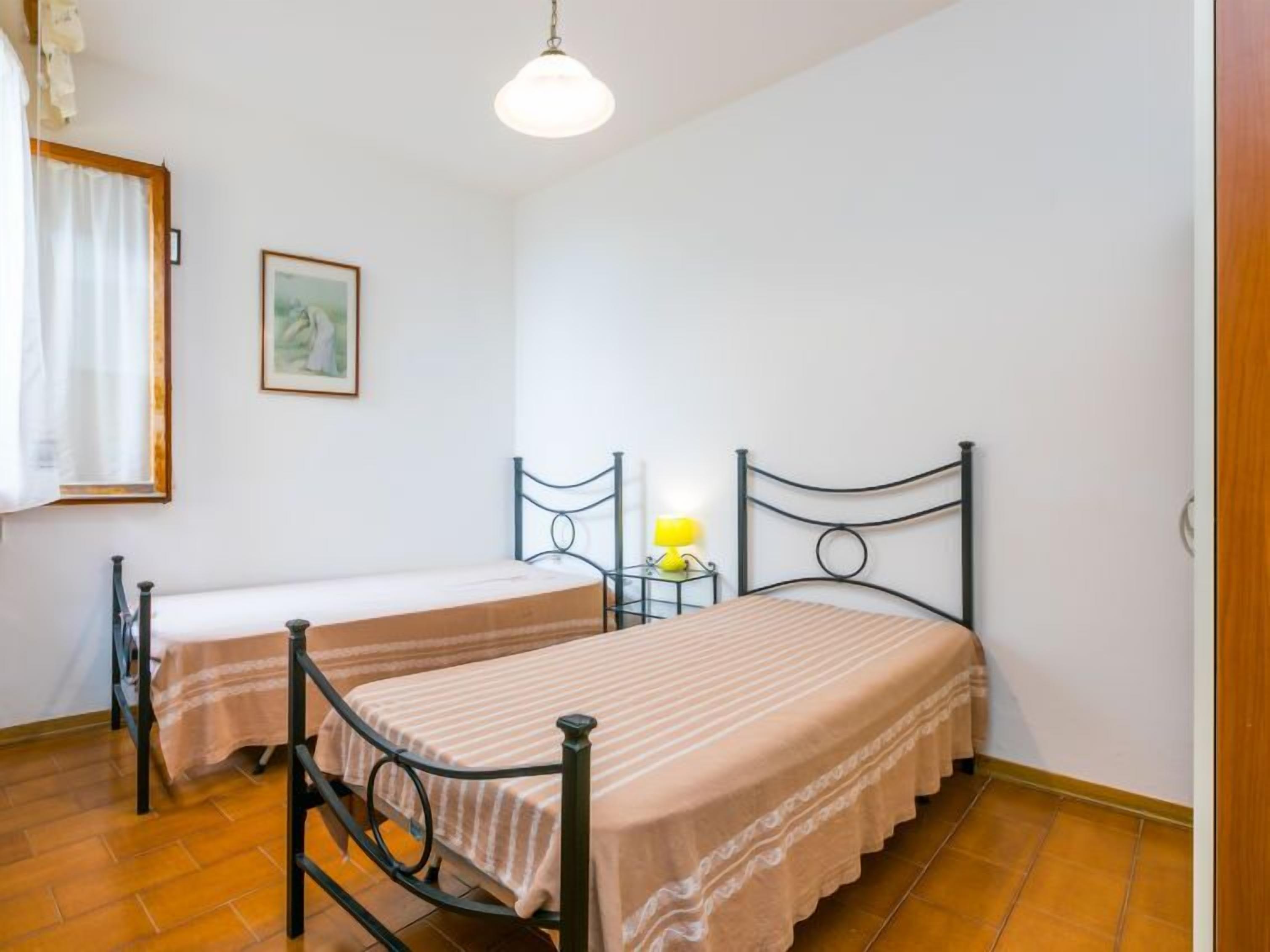 Una camera con due letti singoli, un comodino con una lampada, un quadro appeso al muro e una finestra con tende.
