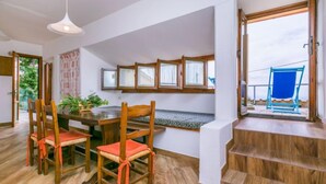 Zona pranzo con tavolo e sedie in legno, lampadario e vista sull'esterno attraverso una finestra.