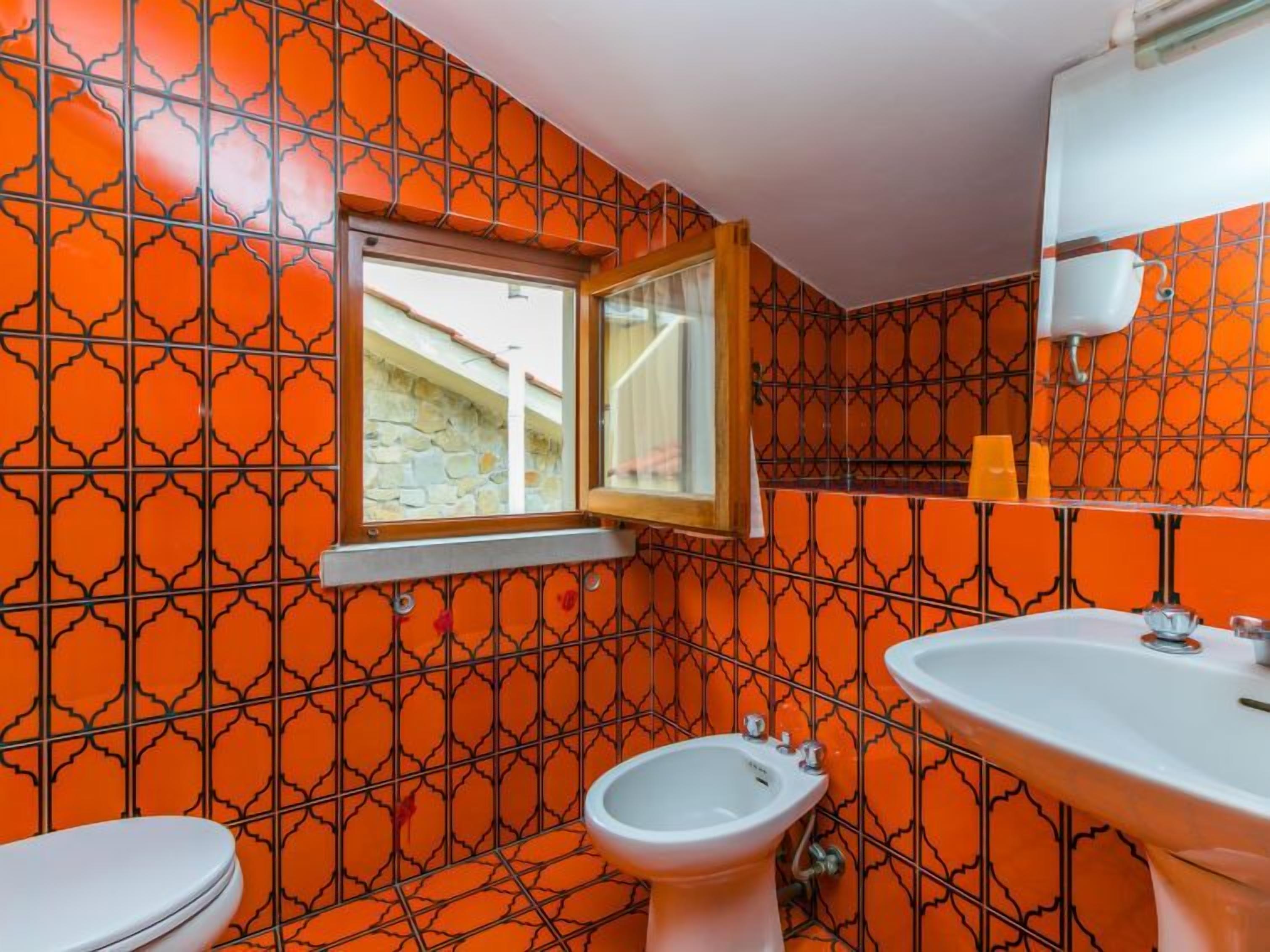 A bathroom with a patterned orange tile wall, a window, a bidet, and a sink.