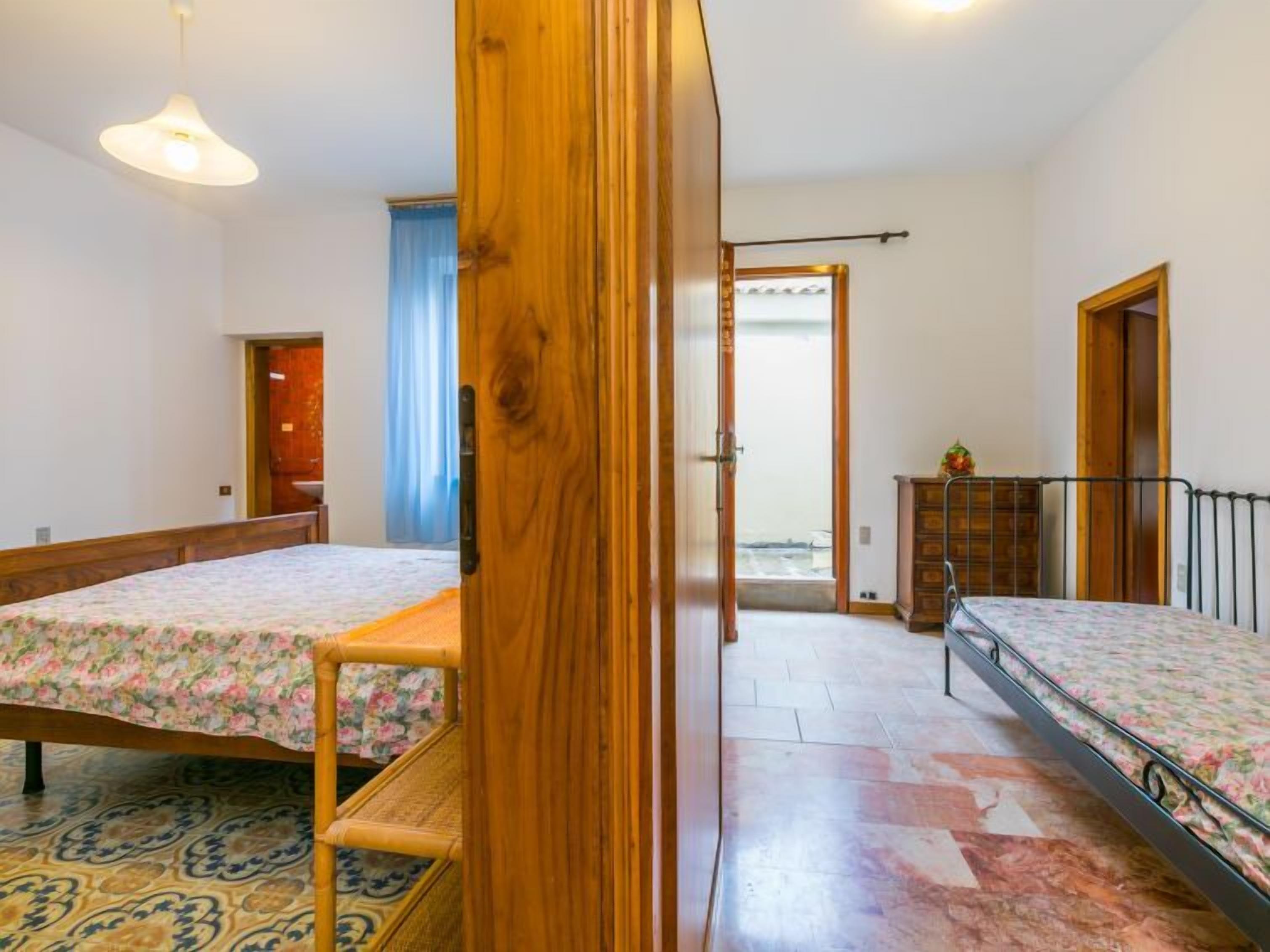 A room with two beds, a wooden wardrobe, a small table, and a hanging light fixture.