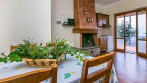 Un coin repas avec une table dressée pour deux personnes, une cheminée en briques et une vue à travers une porte vitrée.