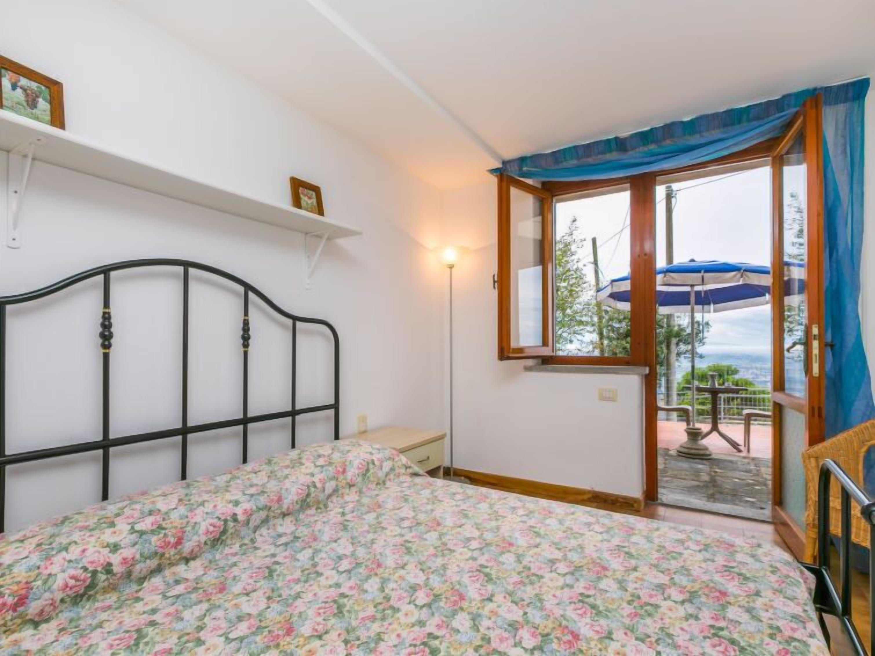 A bedroom with a bed, a nightstand, a window with a view, and a door leading to an outdoor area.