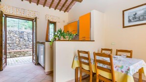 Un coin repas avec une table dressée pour quatre personnes, des chaises en bois et un espace cuisine avec des placards orange et une fenêtre.