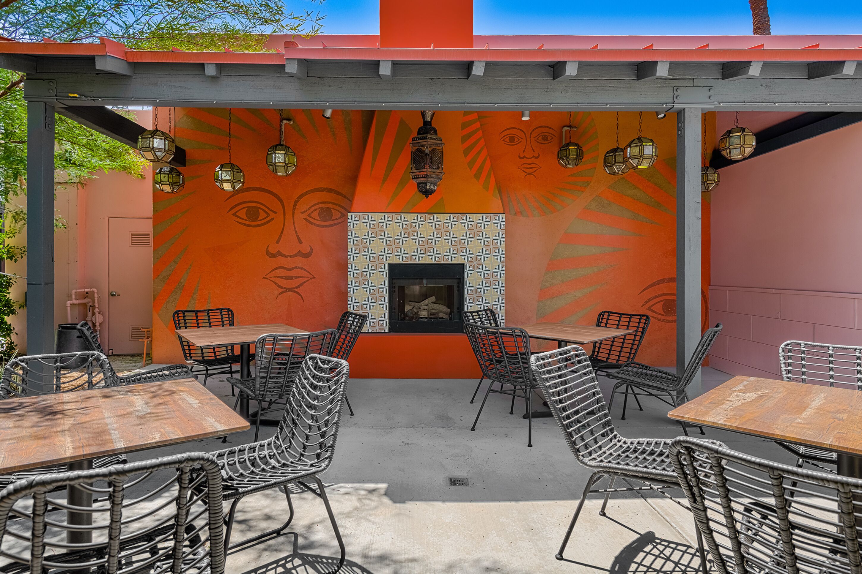 An outdoor patio with tables and chairs, a tiled fireplace, and a mural on the wall.