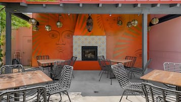 Un patio al aire libre con mesas y sillas, una chimenea de azulejos y un mural en la pared.