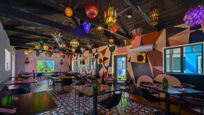 A restaurant with multiple tables and chairs, geometric patterned walls, and hanging decorative lights. - The Paloma Resort (Cathedral City)
