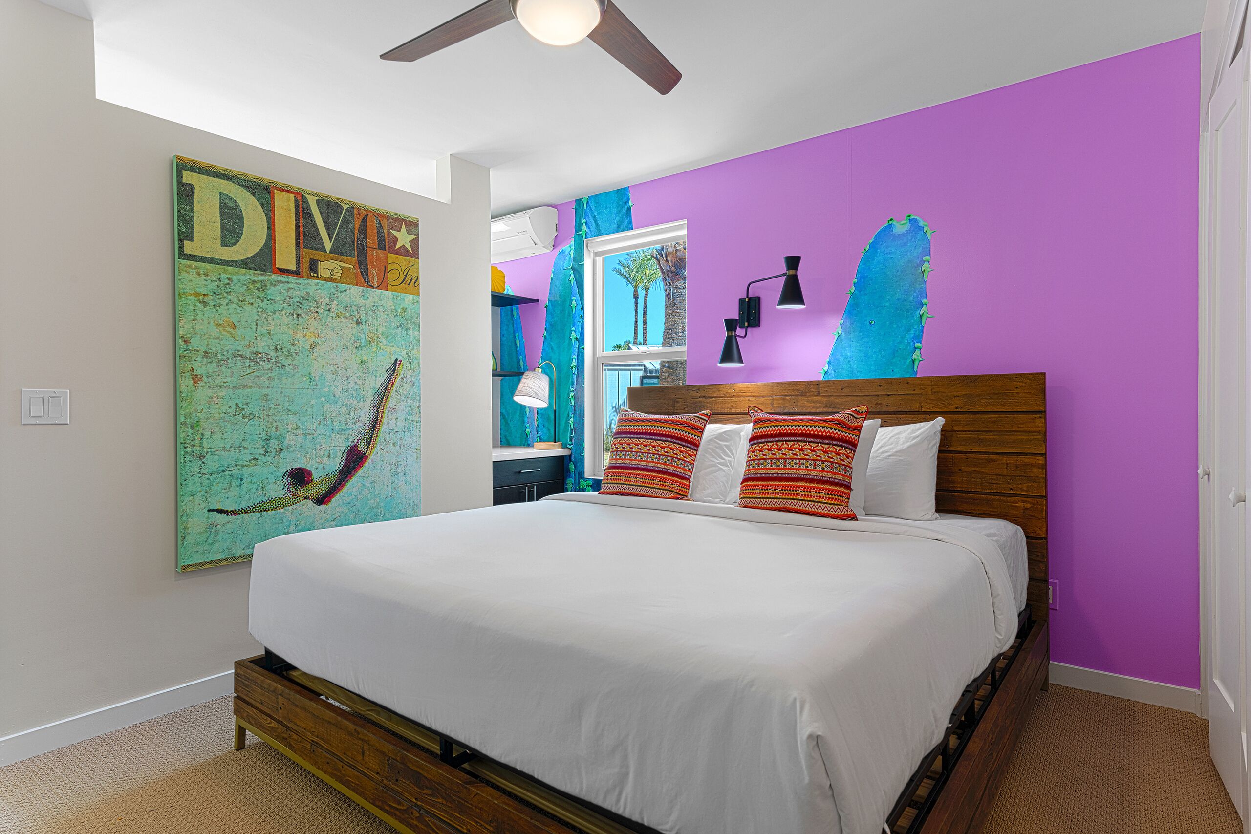 A bedroom with a wooden bed, white bedding, a ceiling fan, and a large wall painting.