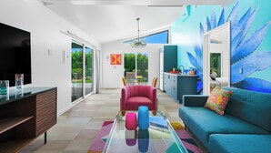 A modern living room with a glass coffee table, a red sofa, and a teal sofa with a colorful pillow. - The Paloma Resort (Cathedral City)