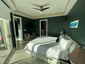 A bedroom with a bed, a ceiling fan, a TV, and a painting on the wall.