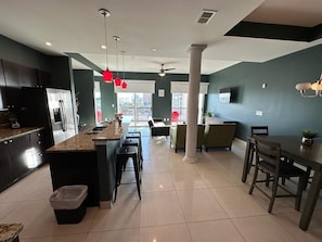 A modern kitchen with a central island, a dining area with a table and chairs, and a view of the outside balcony.