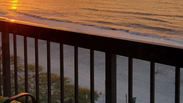 Ein Balkon mit Blick auf den Sonnenuntergang über dem Meer, inklusive Tisch und Stühlen.
