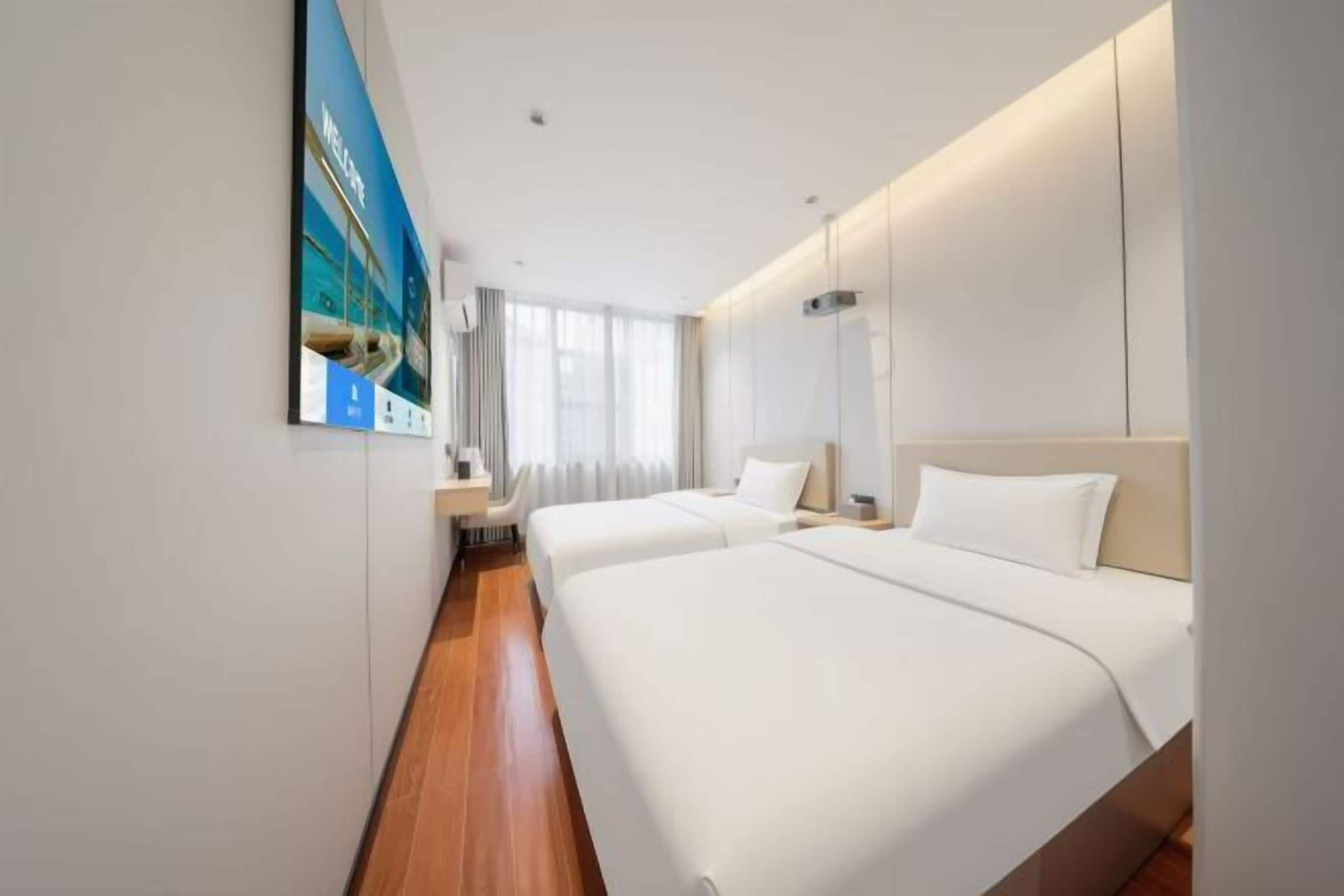 Quarto de hotel com duas camas, uma janela grande e um quadro na parede.